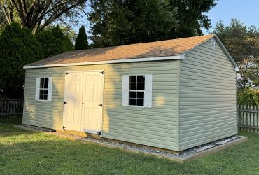 sage green shed pictured from a side angle, lighted with summer sunshine.